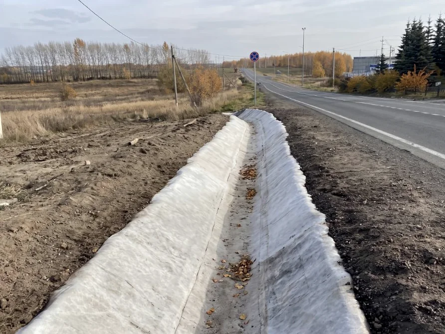 A finished roadside ditch lining, dry and cured, with leaves collected in the invert