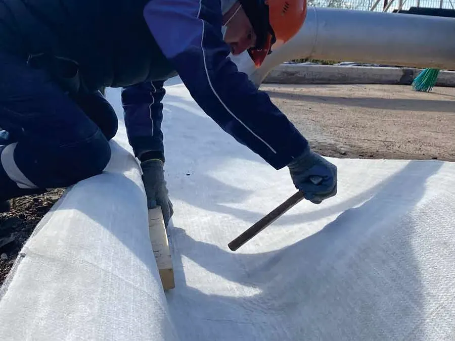 A worker driving a steel anchor through the laid sheet with a hand tool