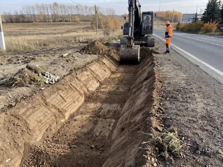 An excavator grading the profile of a roadside drainage ditch before any lining is laid