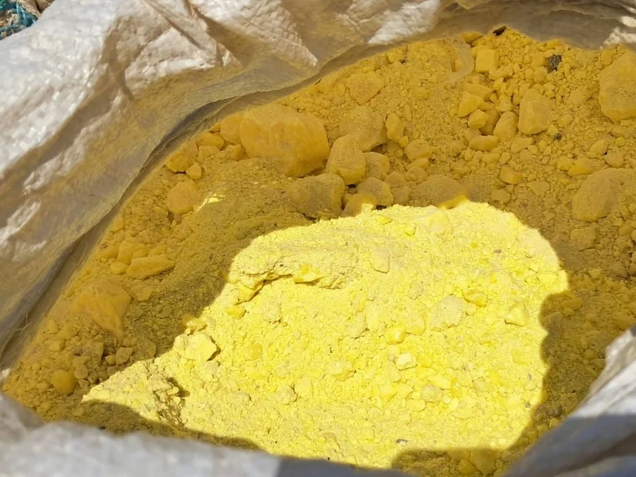 Open bag of sulphur, dull mustard powder with a bright freshly broken face catching sunlight
