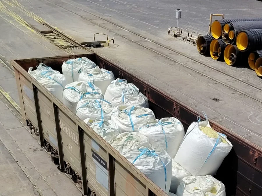 Open railway wagon loaded with big bags of sulphur, one bag open showing pale yellow granules